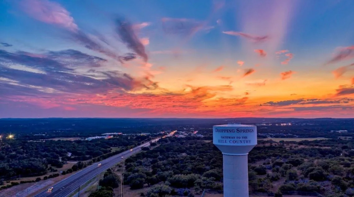 a sunset over a highway with a sign and a highway sign of Dripping Spring