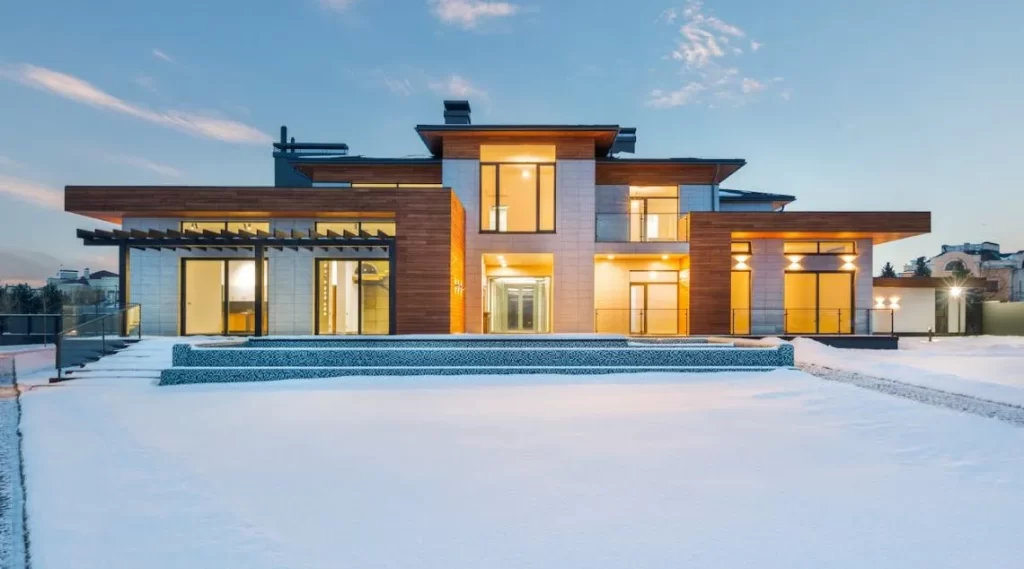 a modern house in the snow with lights on inside the house