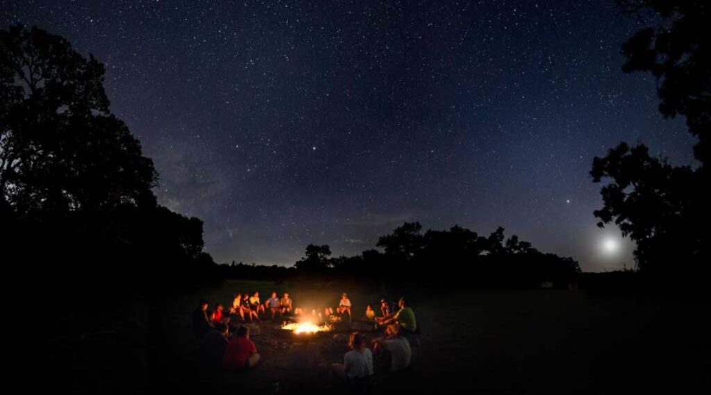 A group of individuals gathered around a campfire, sharing stories and enjoying the warmth of the flames at night.