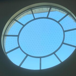 A round window framed against a backdrop of a clear blue sky, creating a serene and open atmosphere.
