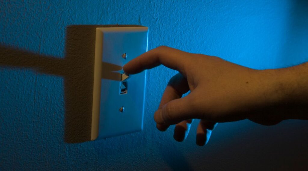 A hand turning off the light with blue light in the background